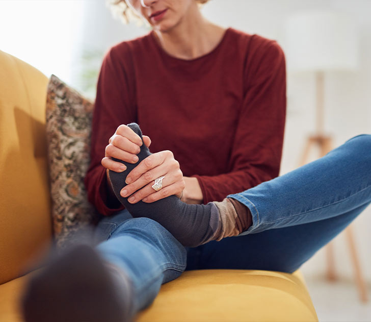 A woman sitting on the couch with her foot in her sock.