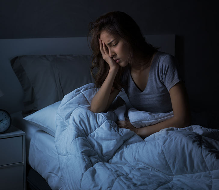 A woman is sitting in bed with her head on the pillow.