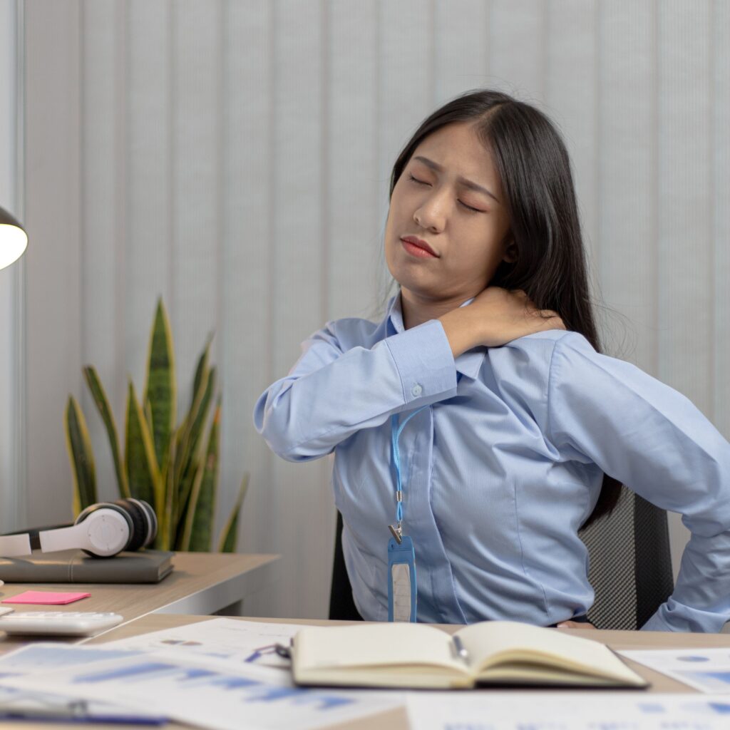 A woman sitting at her desk with one hand on the back of her neck.